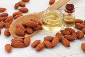Almond oil in a bottle and almond seeds which is recommended as a good light oil for low porosity hair.